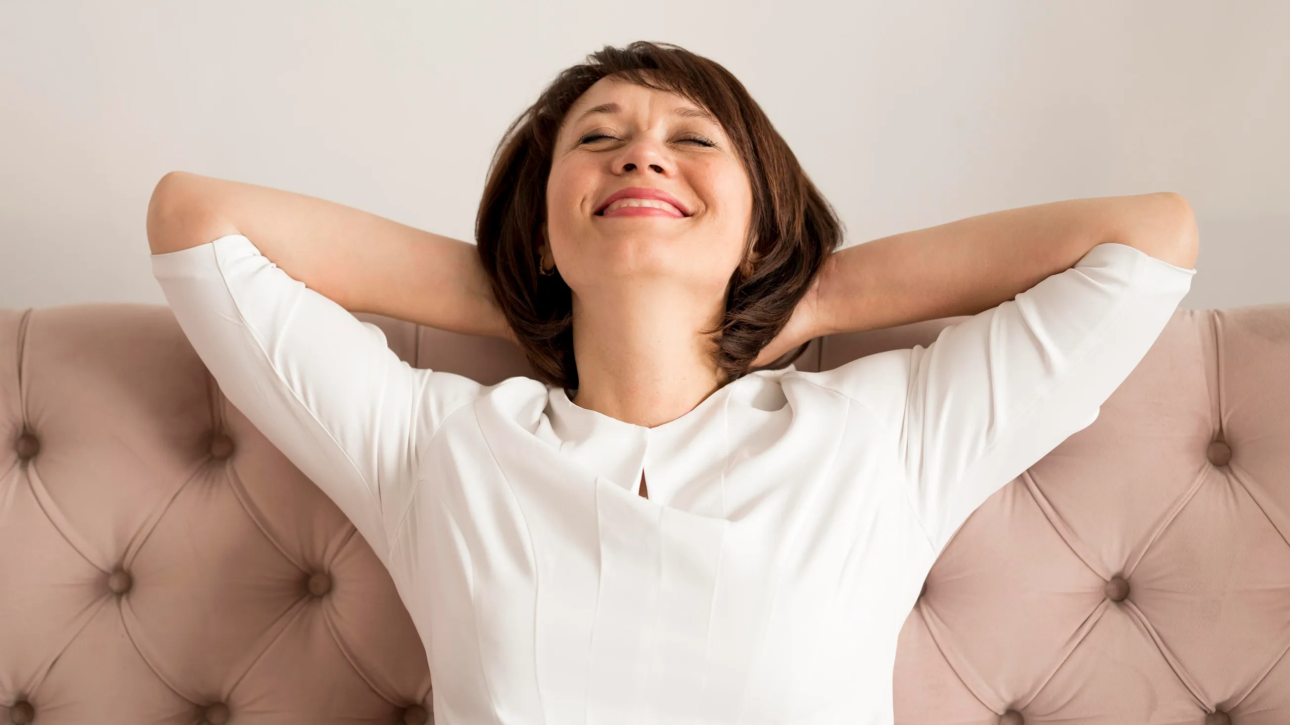 Femme détendue, souriante, les yeux fermés, les mains derrière la tête lors d'un moment de relaxation